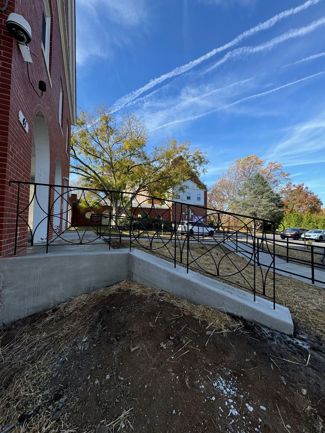 Exterior of a brick building with a concrete ramp and decorative black metal railings. 