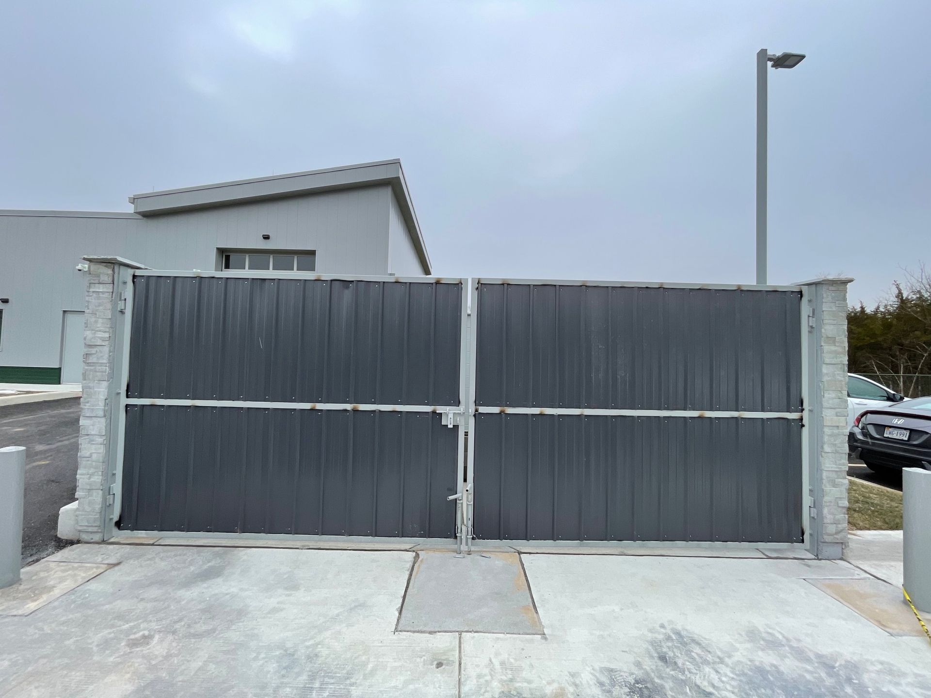 Gray metal gate with concrete posts, in front of a white building under a cloudy sky.