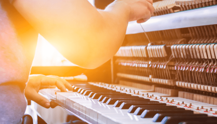 A piano technician tuning an upright piano, adjusting the strings and hammers under warm sunlight