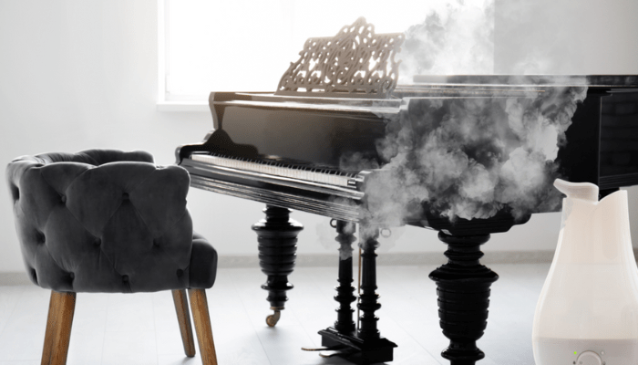 A black grand piano placed in a room with a humidifier releasing steam, demonstrating moisture control to protect the instrument from dry conditions