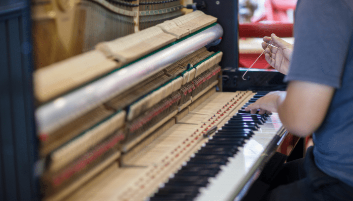 A piano technician tuning an upright piano, using a tuning lever to adjust the strings inside the instrument