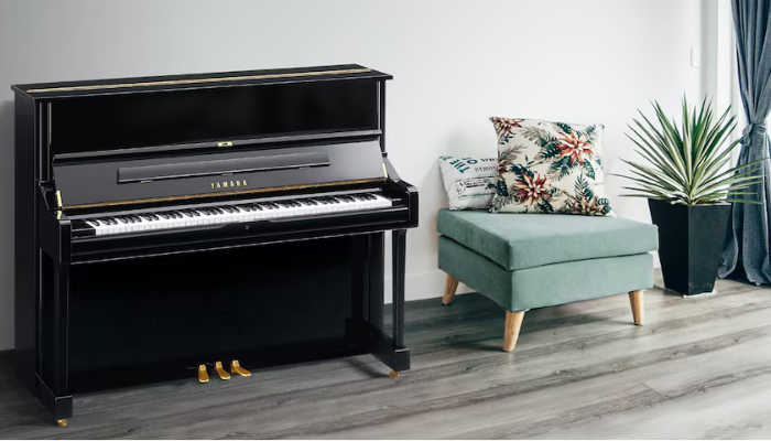 A black Yamaha upright piano placed in a modern living room with a teal armchair, floral cushions, and a potted plant near a window