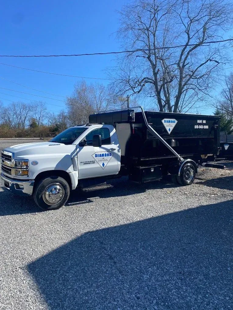 A white commercial dump truck with a black trailer parked on a gravel lot under a clear blue sky.