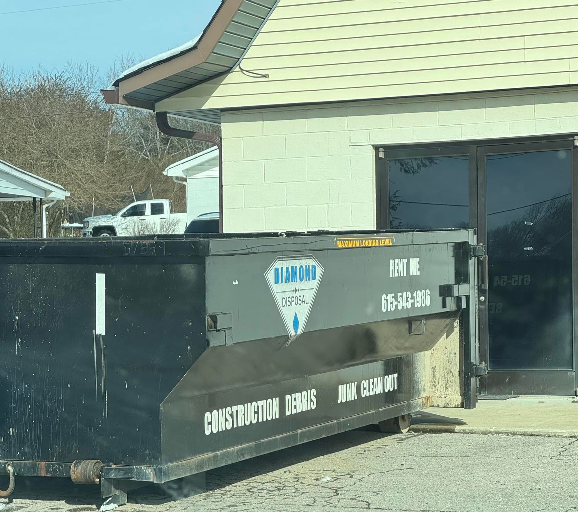 A black Diamond Dumpster container parked outside a beige building.