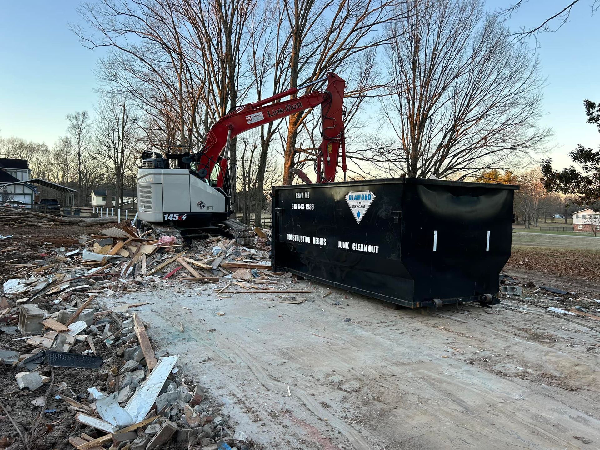 A red demolition excavator parked near a large black dumpster at a construction site littered with debris.