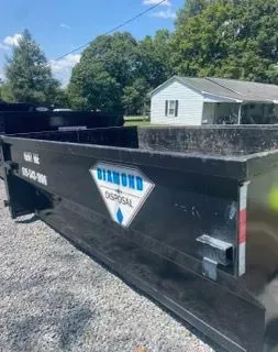 A black Diamond Disposal dumpster sits on a gravel lot in front of a white house.