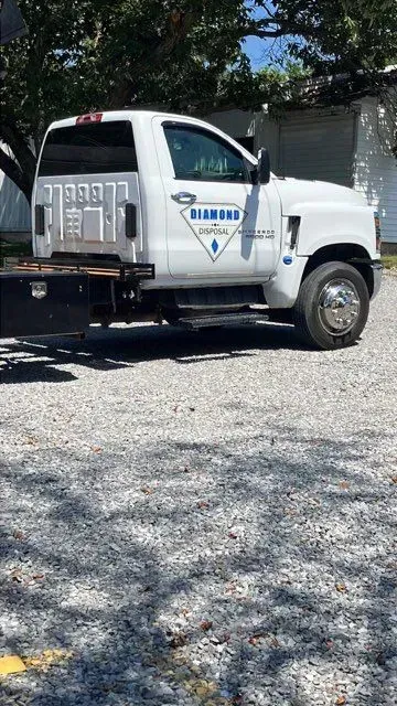 A white service truck with the Diamond logo parked on a gravel lot under the shade of trees.