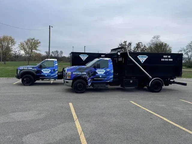 Two Diamond Dumpsters trucks with blue and black branding parked side-by-side in a paved lot.