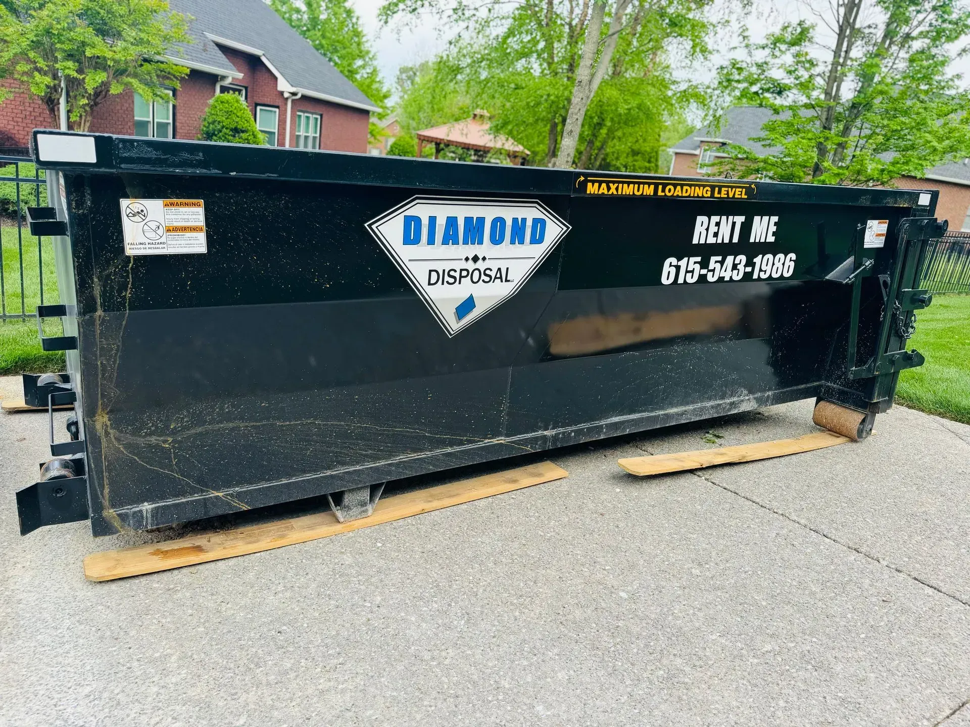 A black Diamond Disposal dumpster sits on a residential driveway, with wooden boards placed underneath it.
