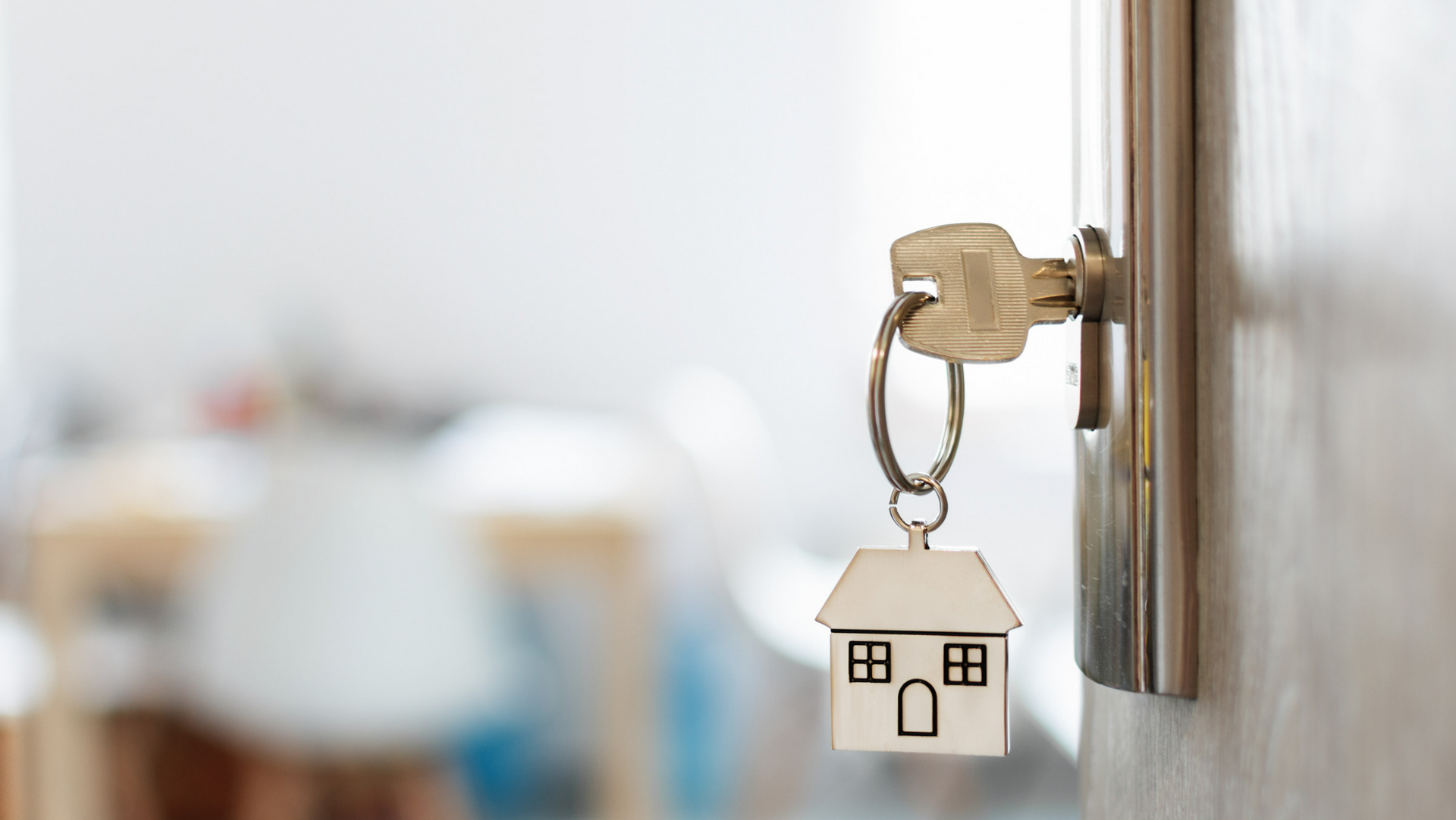 Key in a door with a wood carving of a house as a key chain.
