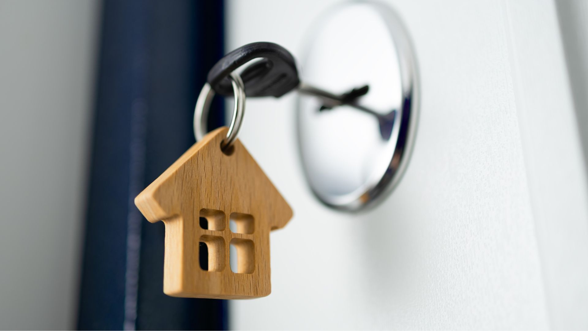 Close-up of a house key with a miniature model home keychain, symbolizing residential leasing and finding a rental property.

