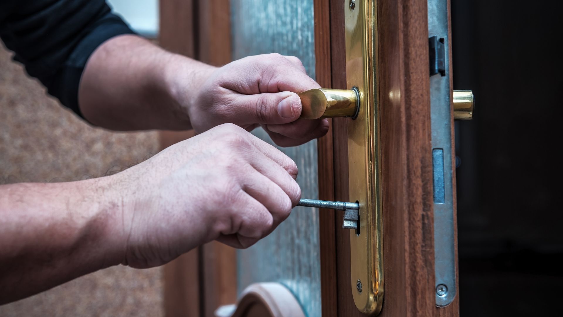 Person using screwdriver on wooden door with brass handle, illustrating locksmithing or lock maintenance task.