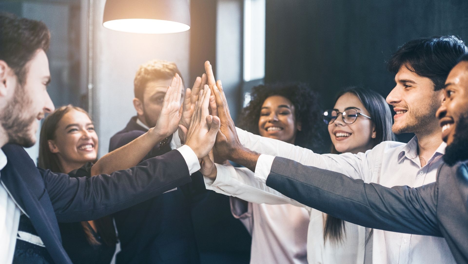 Diverse group of professionals high-fiving in a modern office, showing teamwork and collaboration.