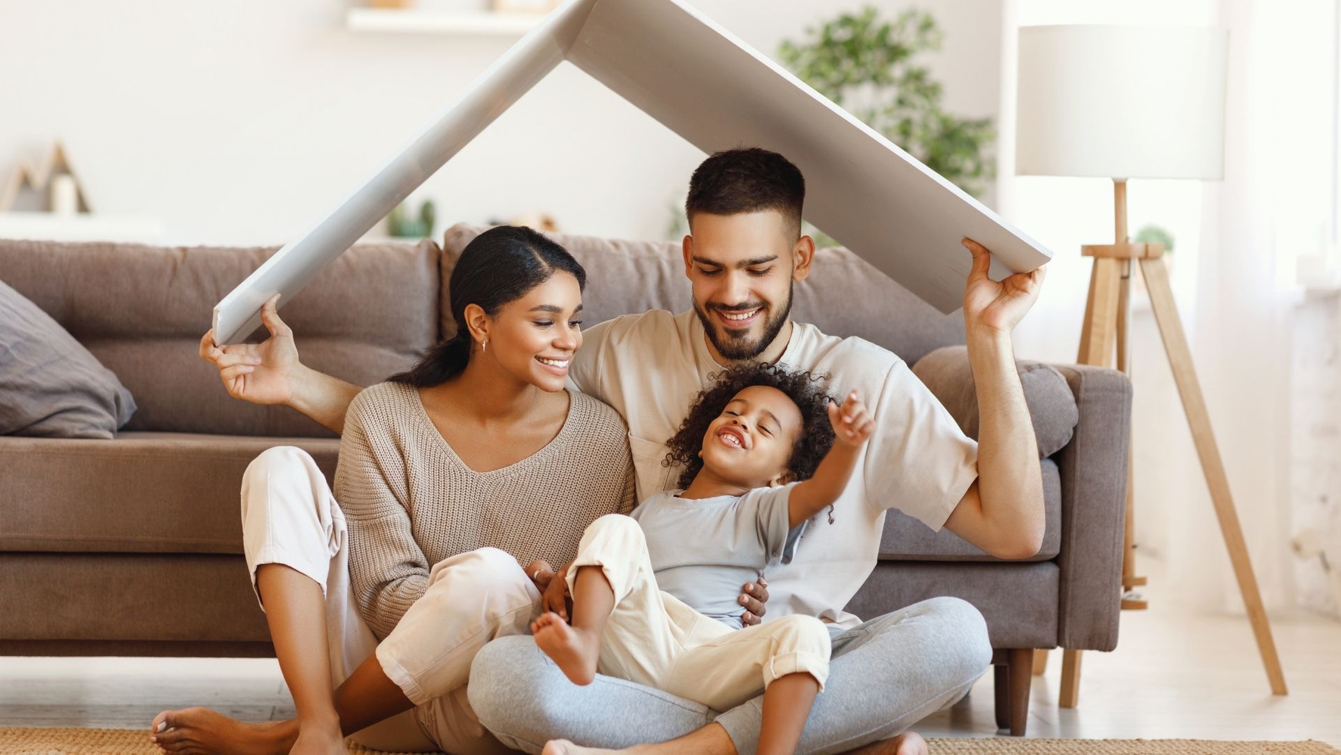 Family sitting together on the floor, holding a cardboard roof above their heads, symbolizing home and protection.