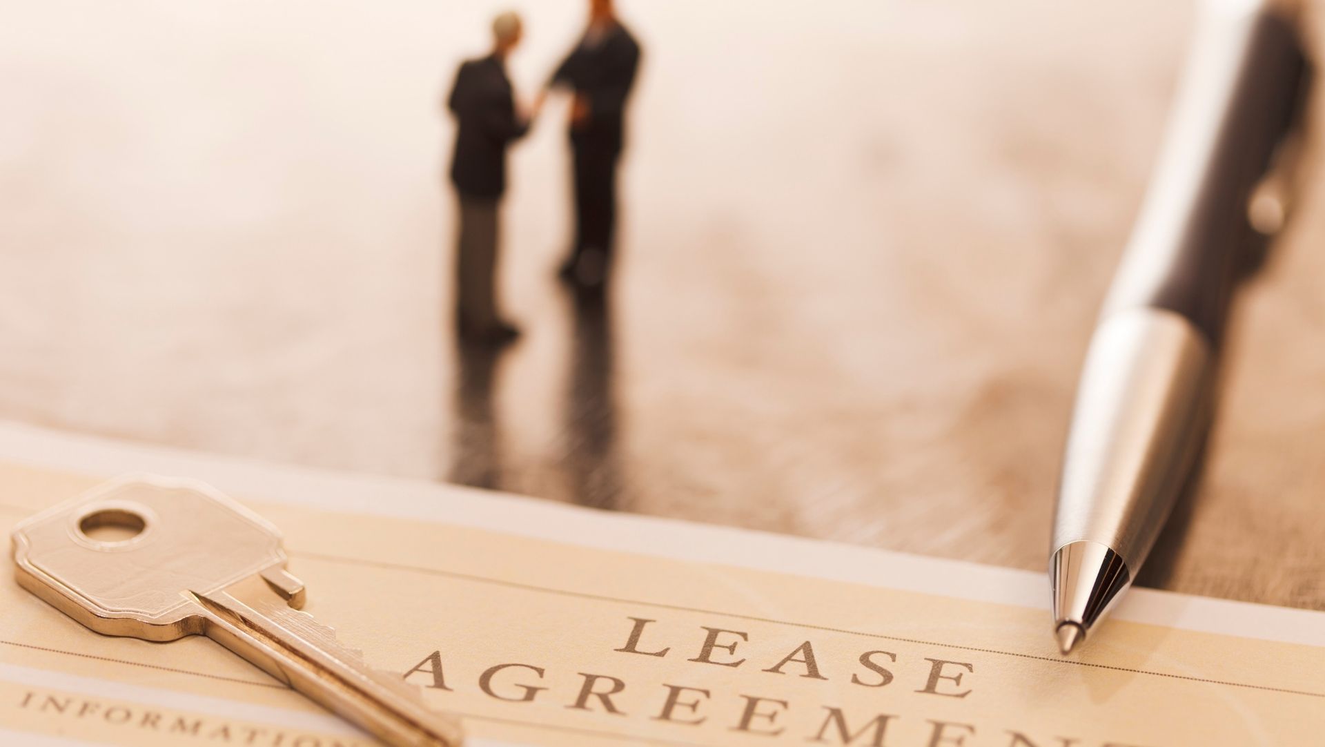 Lease agreement with silver key and pen, blurred handshake in background symbolizing a rental agreement or deal.