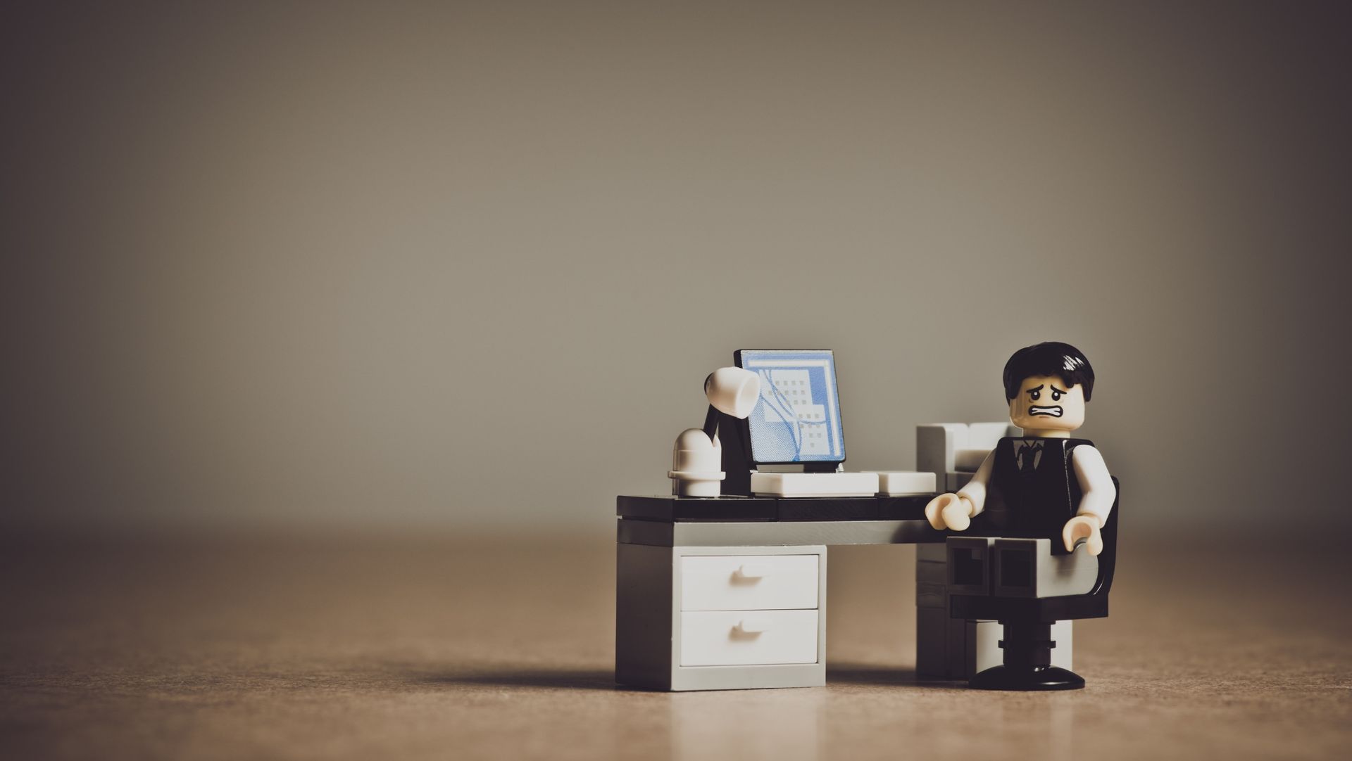 The Lego figure is sitting in a chair at a desk, looking super distraught about the situation.