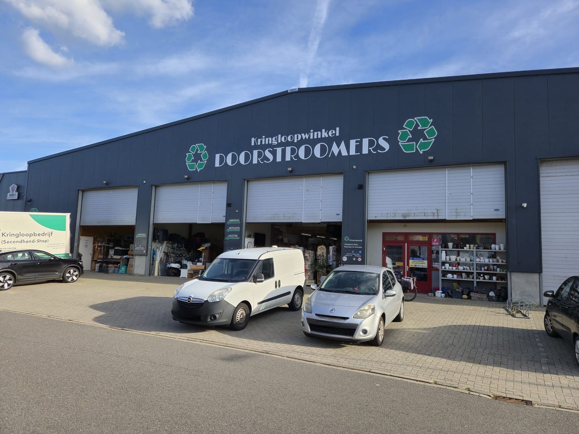 De buitenkant van een kringloopwinkel met open deuren en parkeerplaatsen