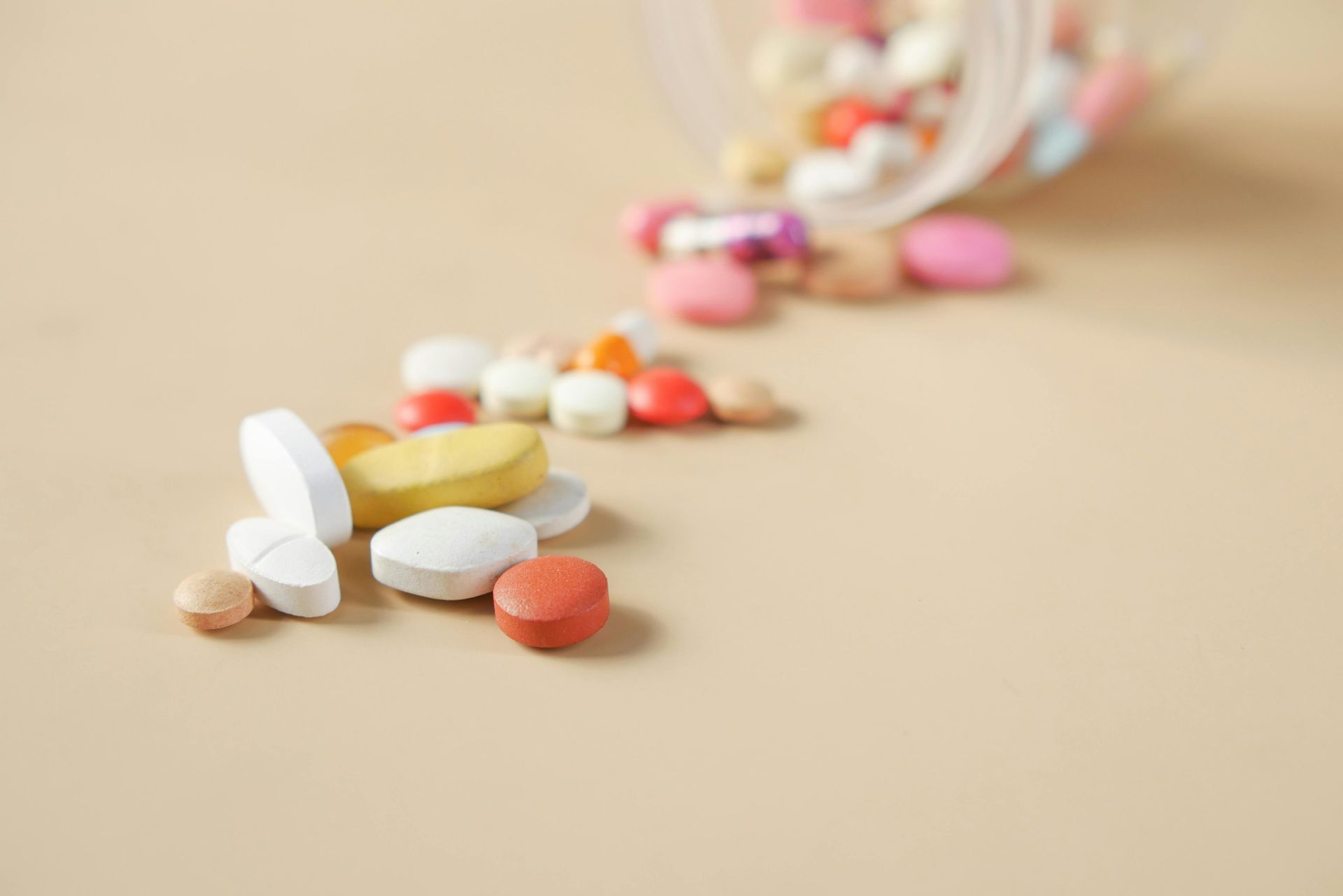 Spilled mixed pills and capsules scattered from a pill bottle on a beige surface