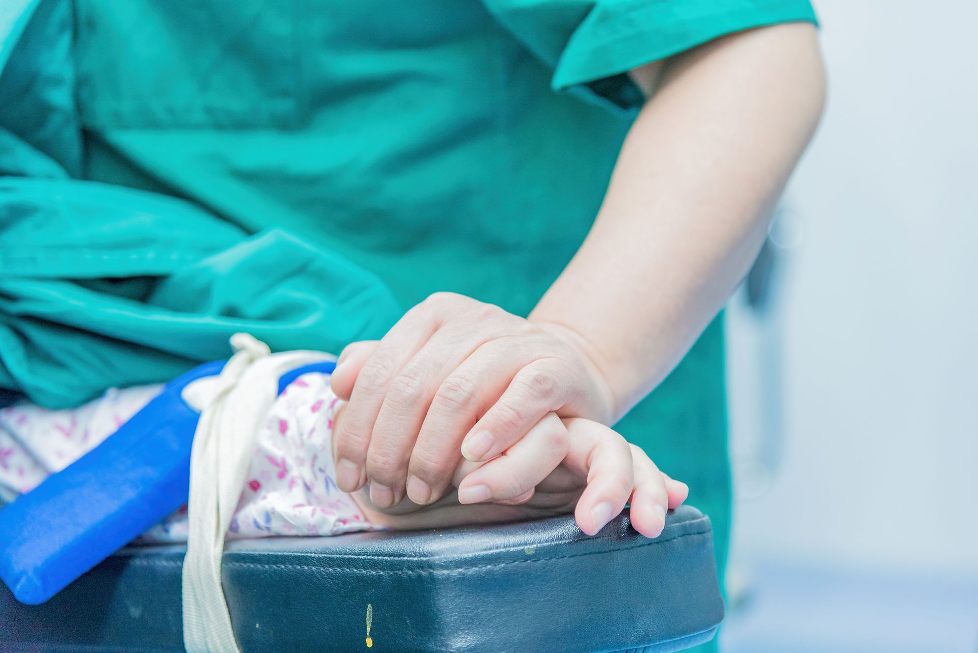 Adult in green scrubs holding a small hand on a padded table during a medical procedure