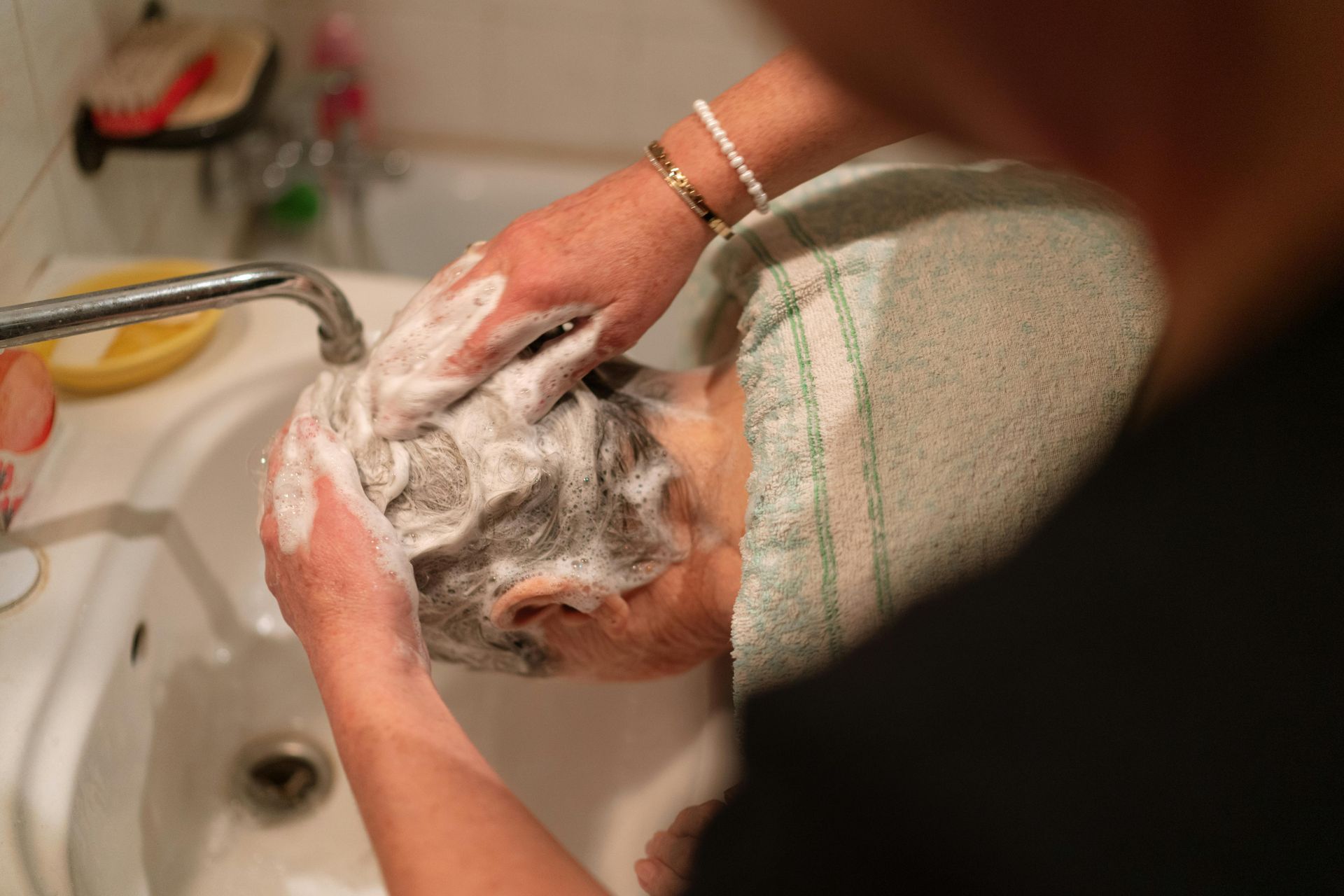 Hands washing a foamy dog under a bathroom faucet.