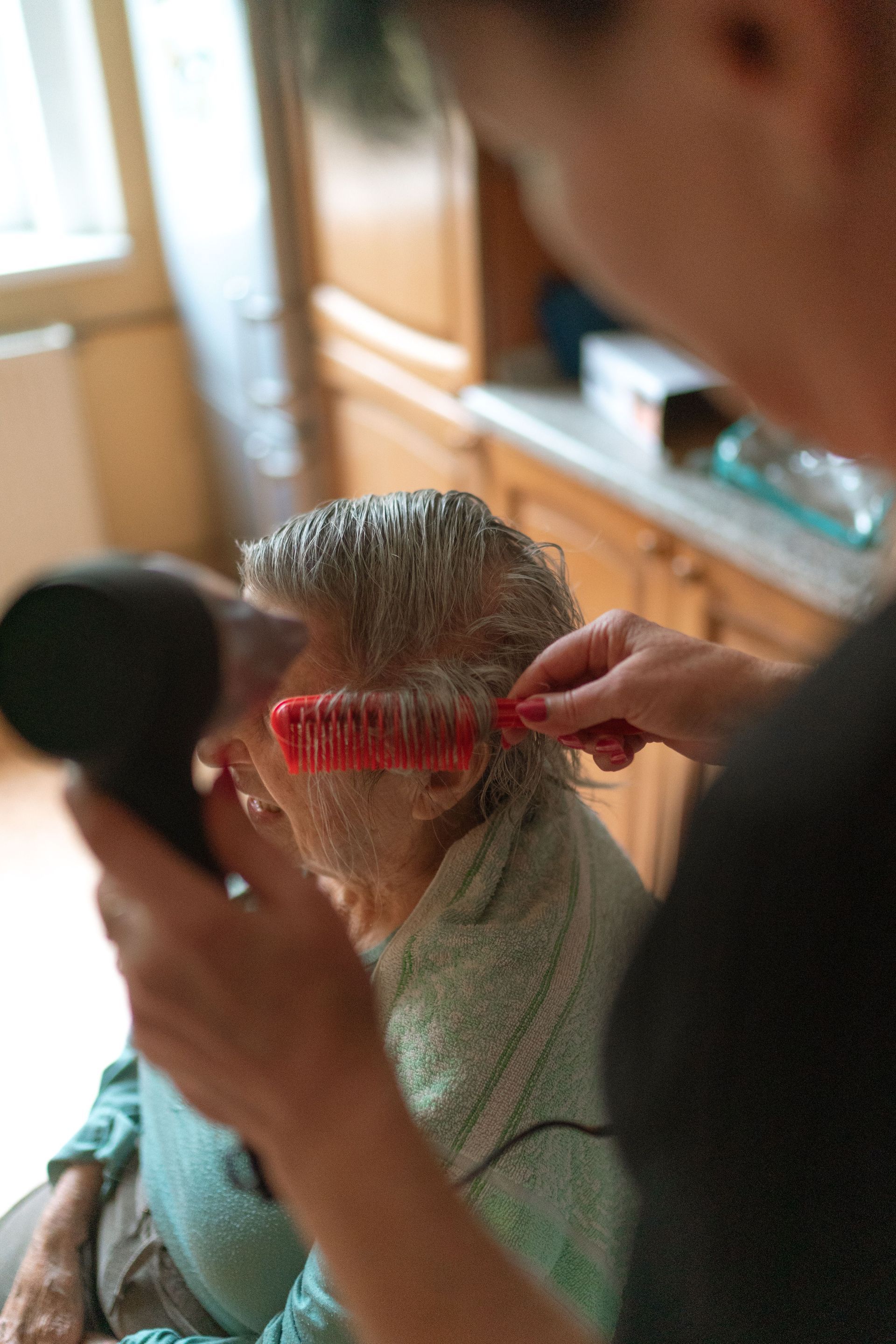 Person combs another person’s gray hair in a salon or home setting.