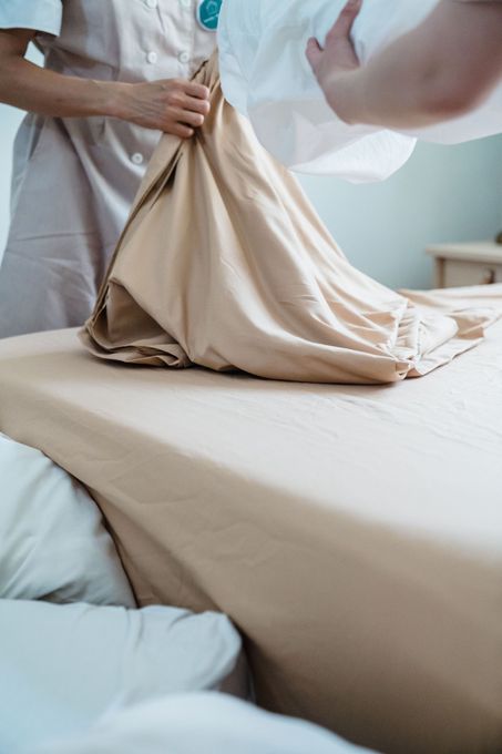 Person changing beige bed sheets in a bright bedroom