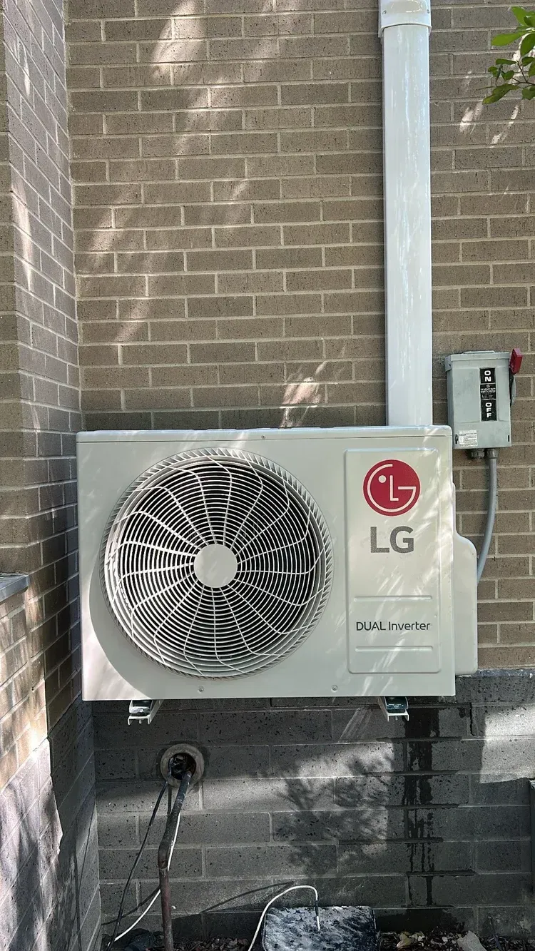 LG outdoor air conditioner unit mounted on a brick wall with metal piping and a conduit box