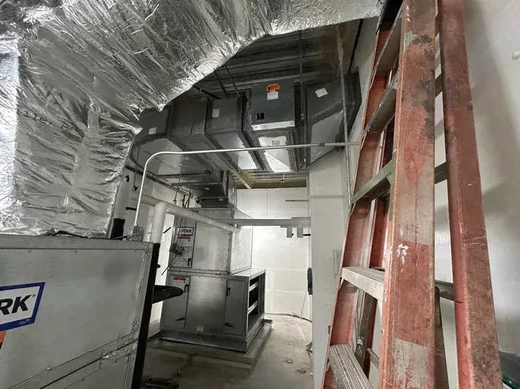Industrial mechanical room with HVAC ductwork, metal equipment, and a red ladder in a narrow utility corridor