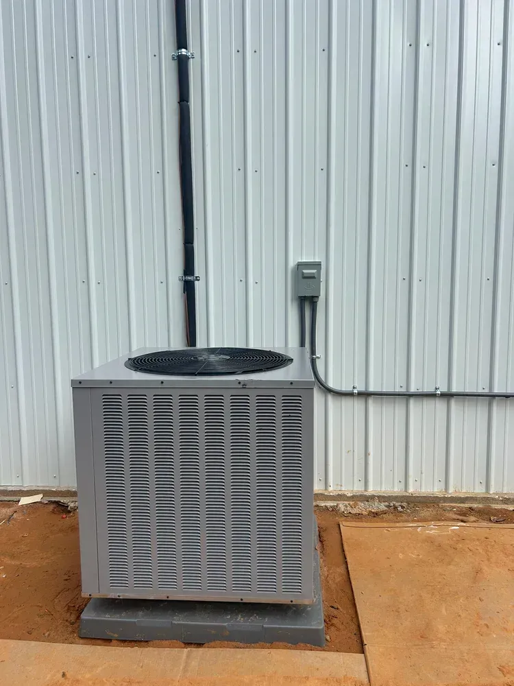 Outdoor air conditioning unit beside a corrugated metal wall with a nearby electrical box.