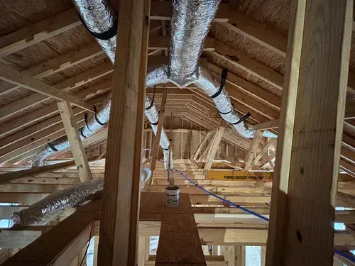 Attic with exposed wooden rafters and silver HVAC ducts running along the ceiling