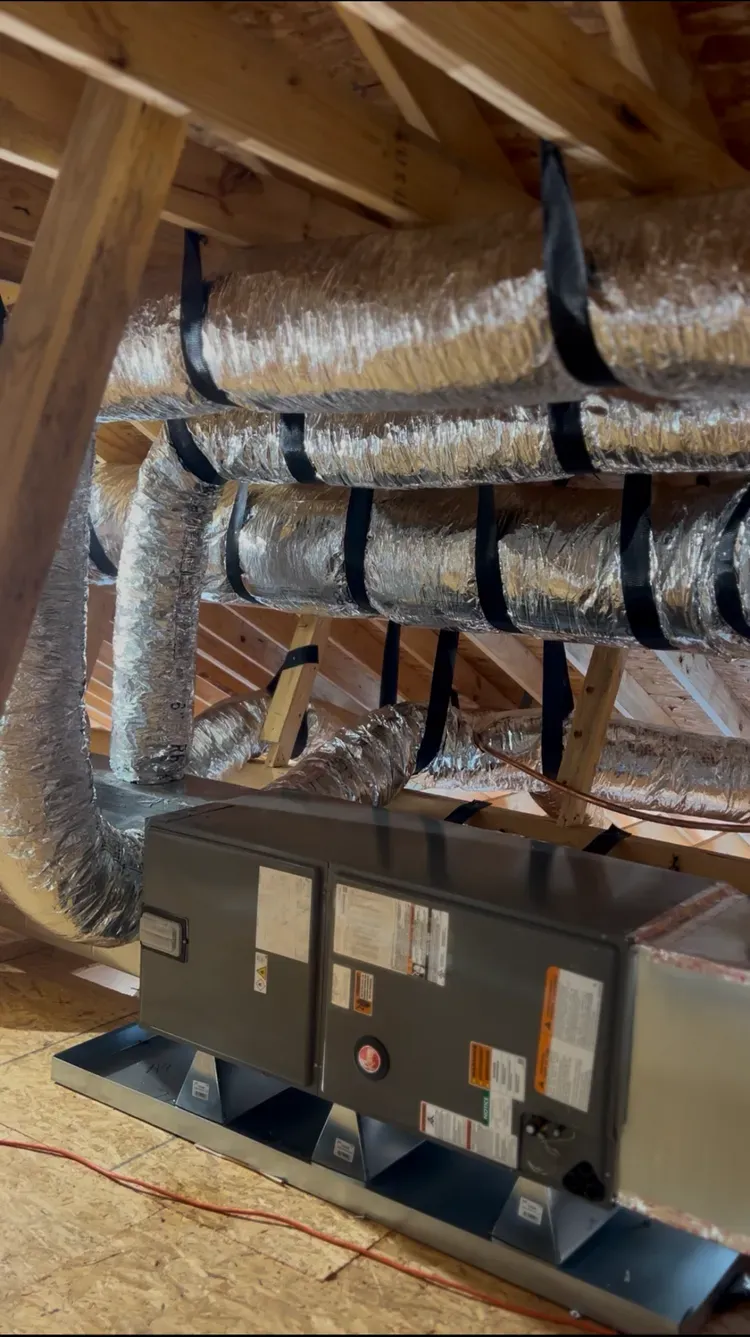 Basement HVAC unit with insulated ductwork under exposed wooden rafters