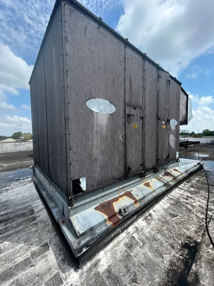 Weathered dark-gray rooftop enclosure with a small oval window and rust-streaked base on a snowy roof