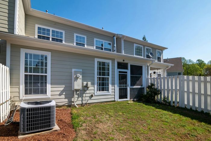 The backyard of a house with a white picket fence and an air conditioner.