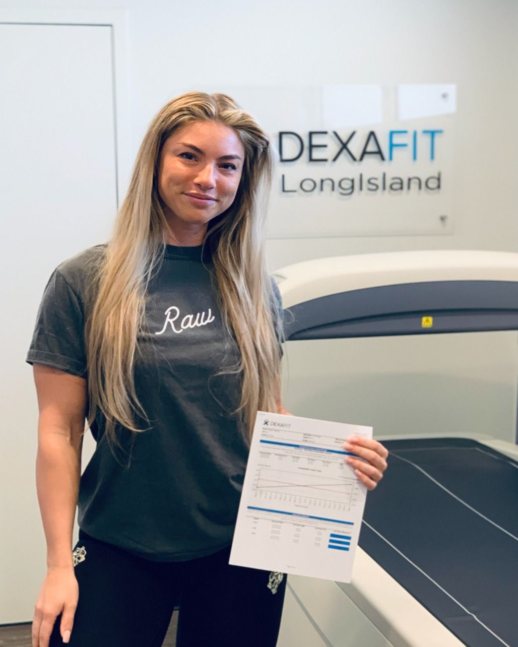 Woman holding a paper stands in front of a DEXA machine
