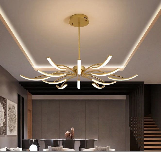 Gold modern chandelier illuminating a room with art, furniture, and stairs.