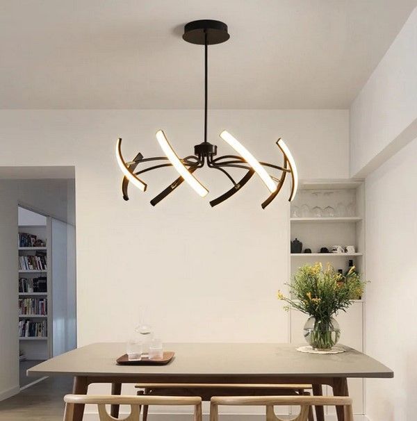 Gold modern chandelier illuminating a room with art, furniture, and stairs.