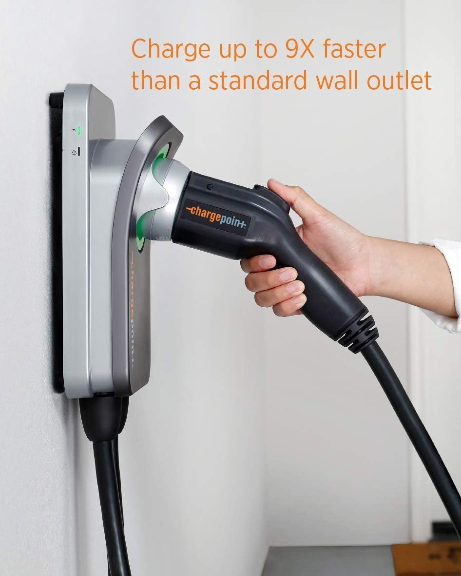 A person plugs an electric vehicle charger into a wall-mounted charging station. The charger is black and green.