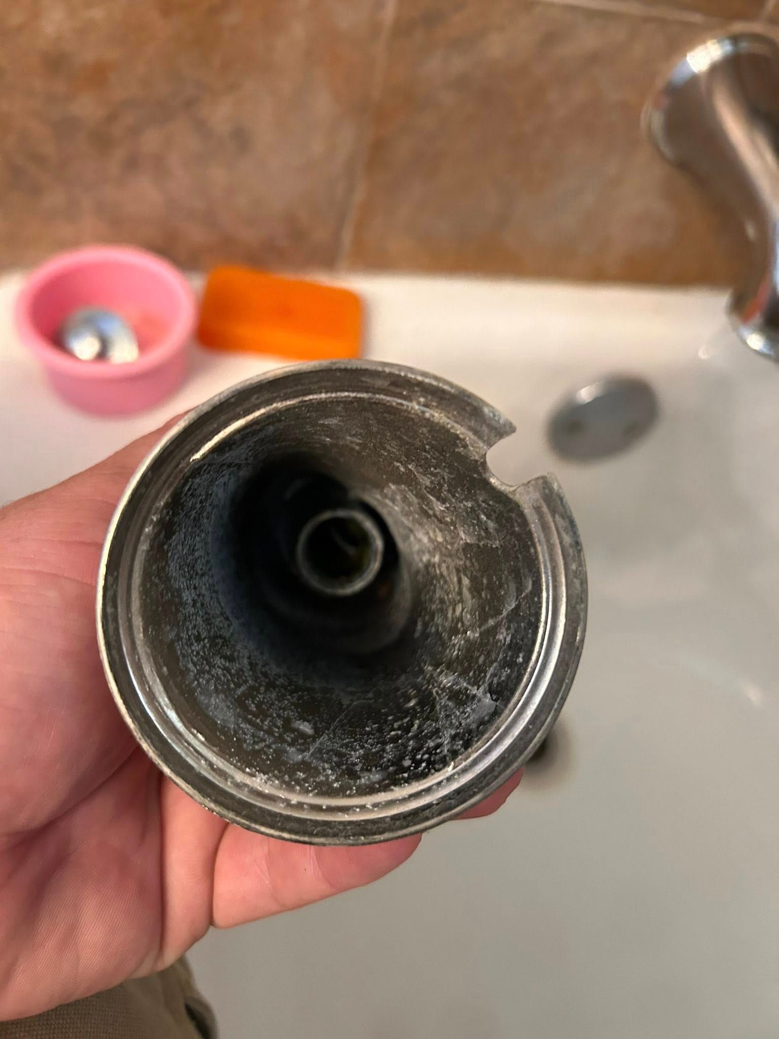 Close-up of a corroded metal showerhead holder, held in a hand, inside a bathtub.