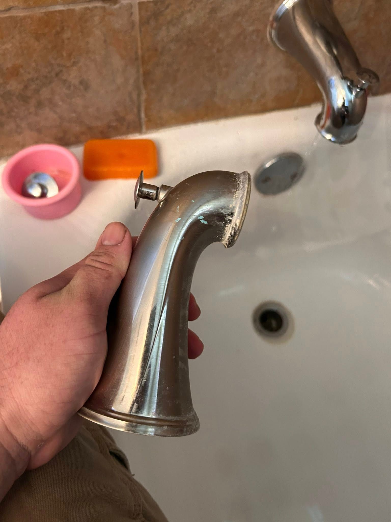 Hand holding a detached silver faucet spout above a bathtub.