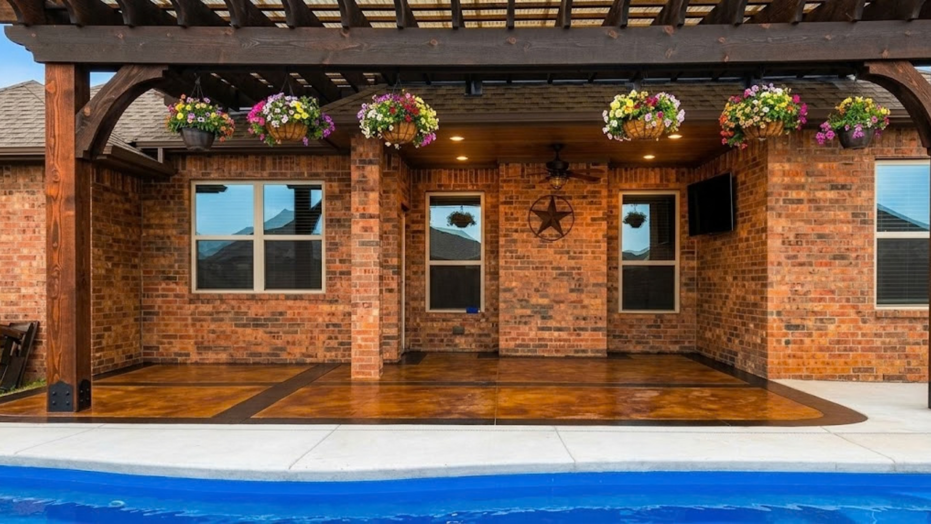 Brick storefront with hanging flower baskets and wooden doors beside a blue pool or walkway