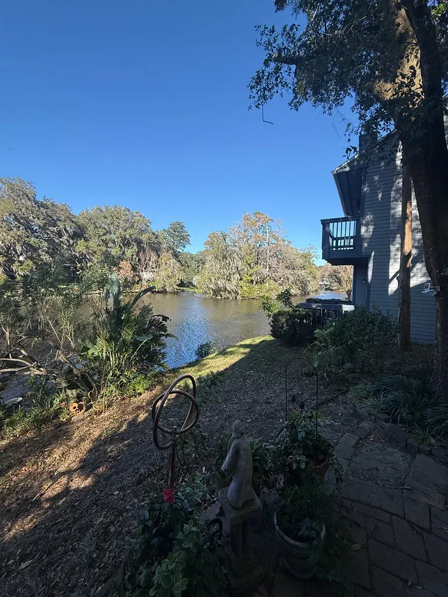 Riverside view with trees, blue sky, and a house balcony overlooking the water