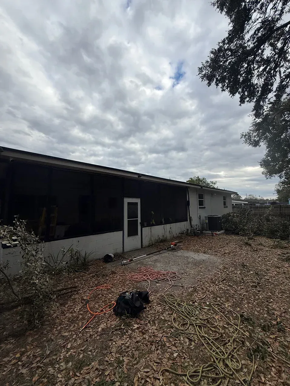 Single-story house with a dark roof, white walls, and a gravel yard under a cloudy sky.