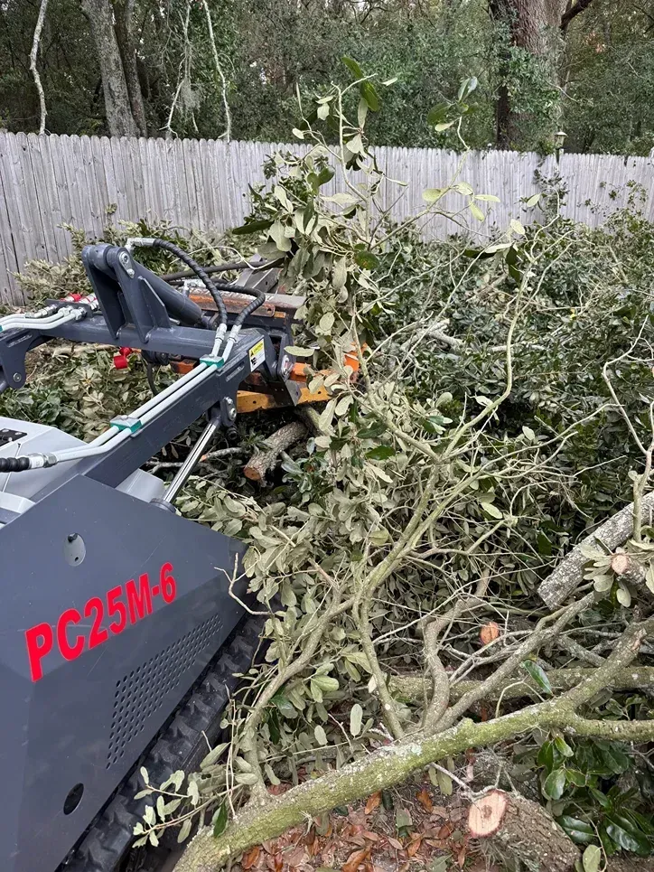Wood chipper clearing a pile of cut tree branches in a backyard beside a wooden fence