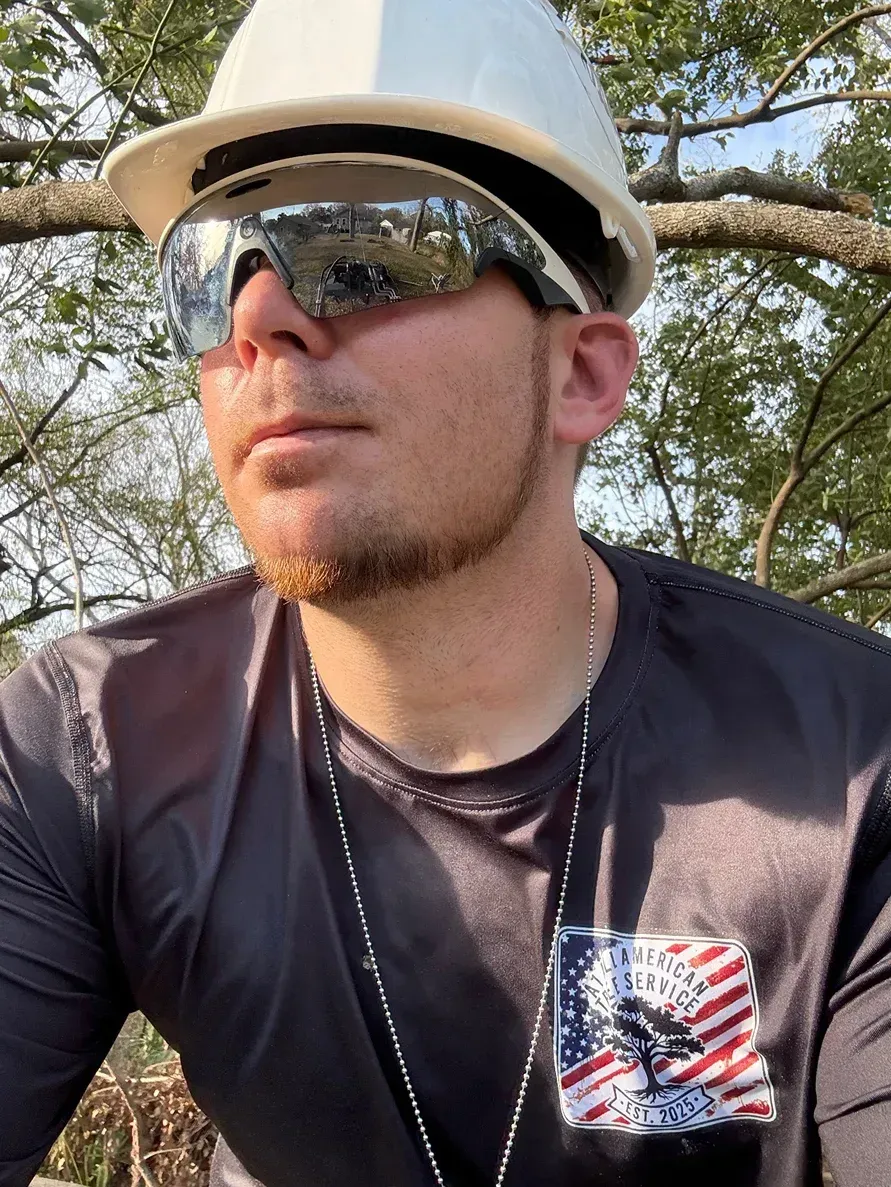 Man wearing a white hat and sunglasses outdoors, looking off to the side in dappled sunlight.