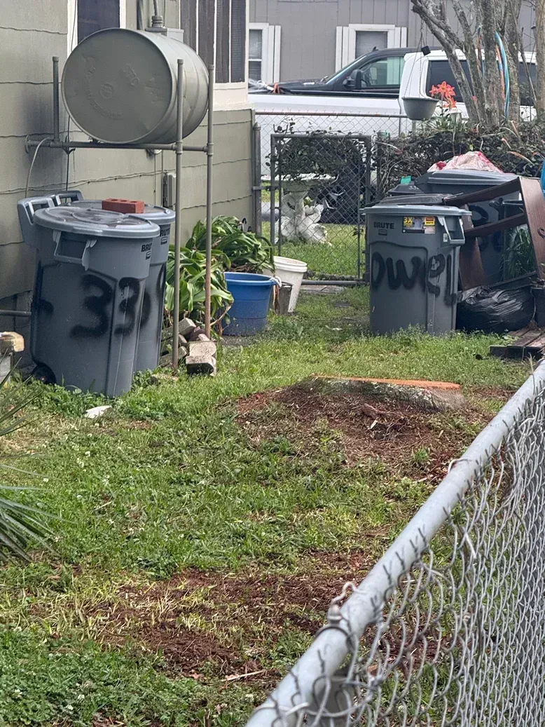 Backyard with two trash bins, a satellite dish, and a chain-link fence beside a grassy yard