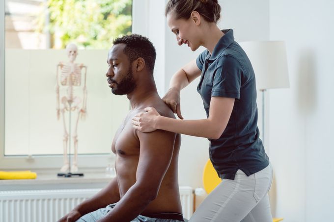 Physical therapist treating a seated patient with shoulder massage in a bright clinic room
