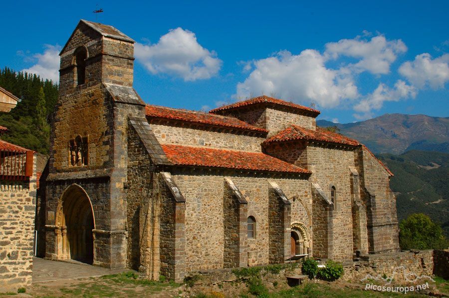 Stone church with red tile roof against a backdrop of mountains and a blue sky with clouds.