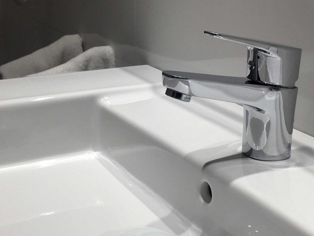 Shiny chrome faucet over a white sink with a rolled white towel visible in the background.