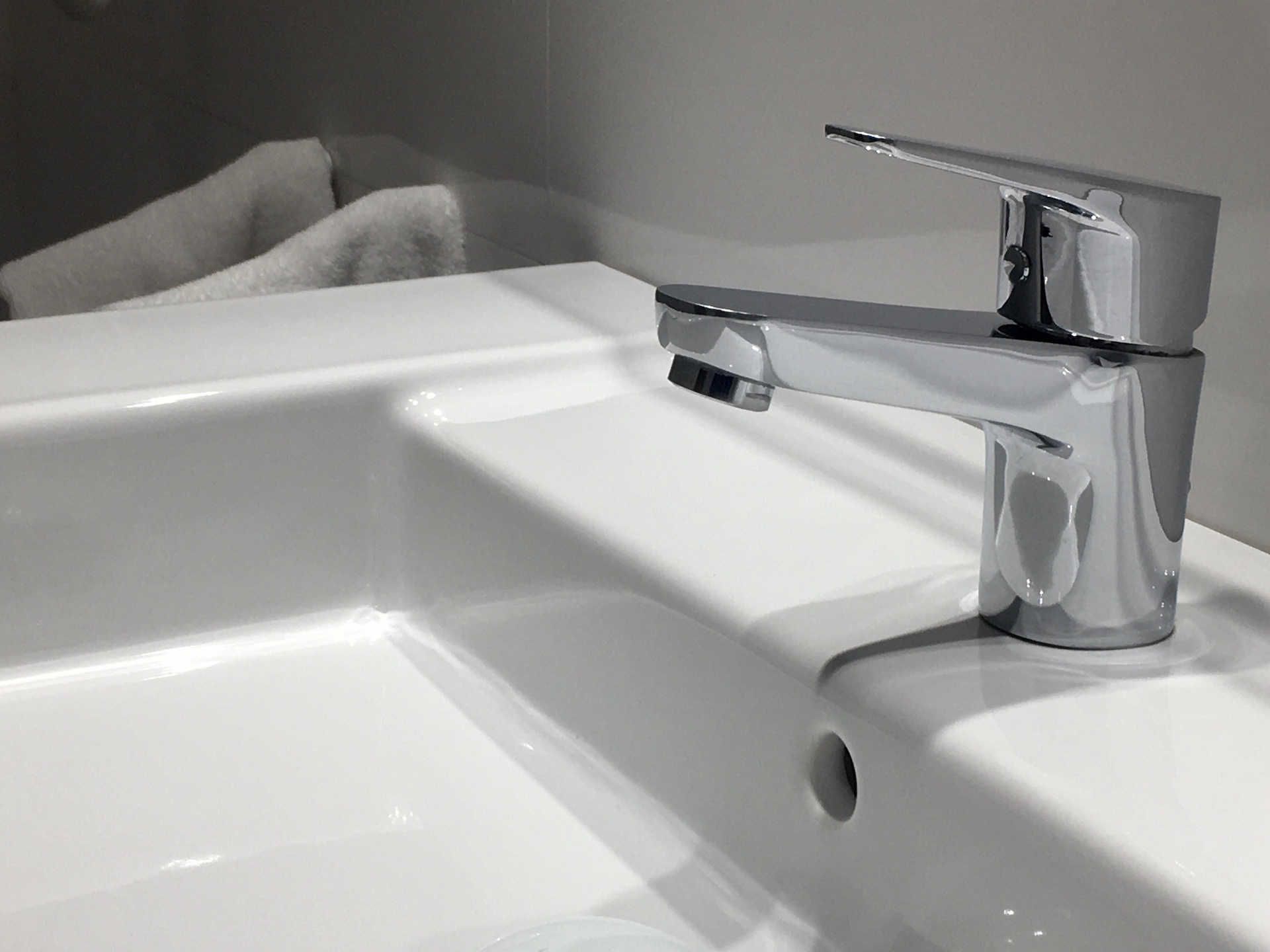 Chrome faucet over a white sink, towel in background.