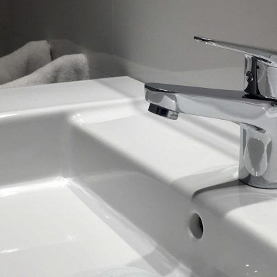 White bathroom sink with chrome faucet. White towels in the background.